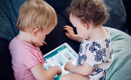 two toddlers both sitting with a tablet between them 